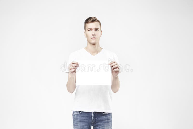Handsome guy standing with blank sheet in hand, isolated on white background, wearing jeans and t-shirt. Free available space for layout text. Handsome guy standing with blank sheet in hand, isolated on white background, wearing jeans and t-shirt. Free available space for layout text