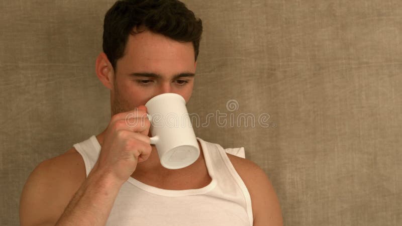 Stiligt mansammanträde på säng som dricker kaffe lager videofilmer