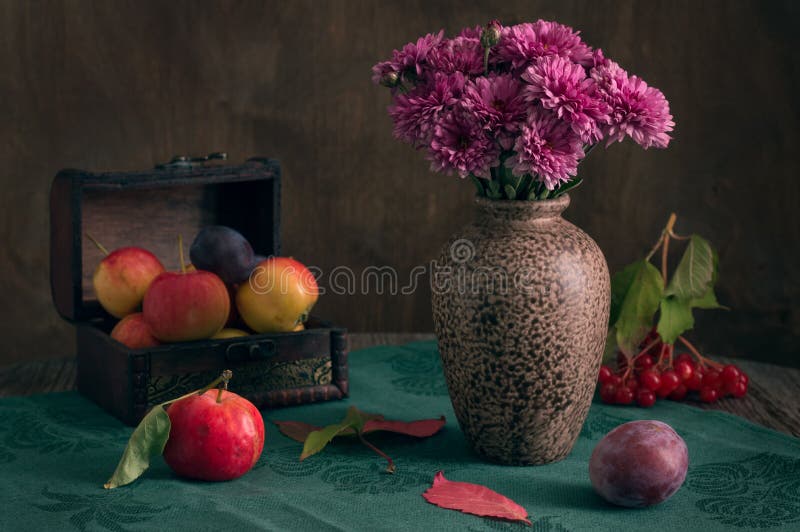 Still life with autumn flowers. Chrysanthemums in a vase on a green tablecloth are decorated with autumn apples and plum.