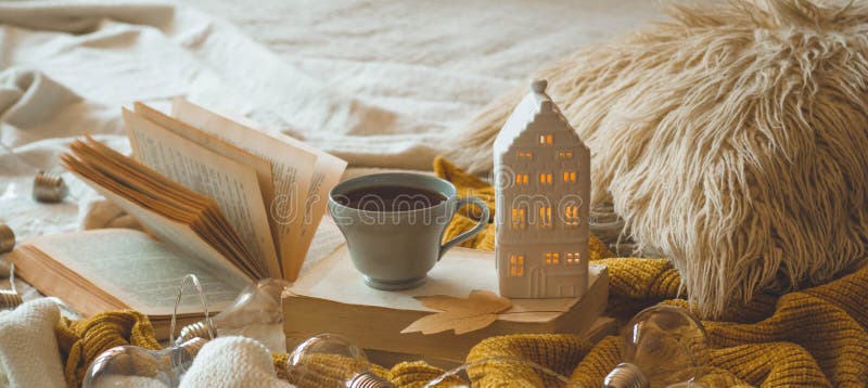 Still life details in home interior of living room. Sweaters and cup of tea with a candle house and autumn decor on the books