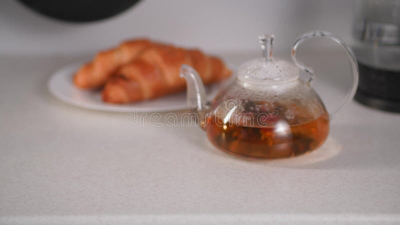 Still life, female hands take transparent cups with delicious healthy herbal tea against the background of a teapot with