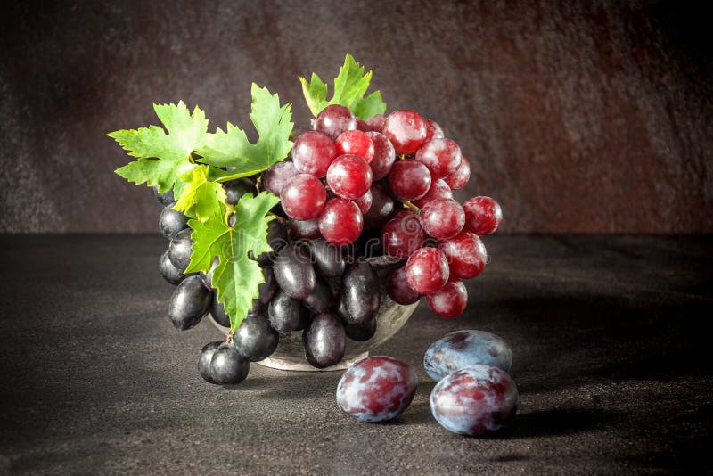 Still life with fruits: grape, plum in the antique copper tin cup