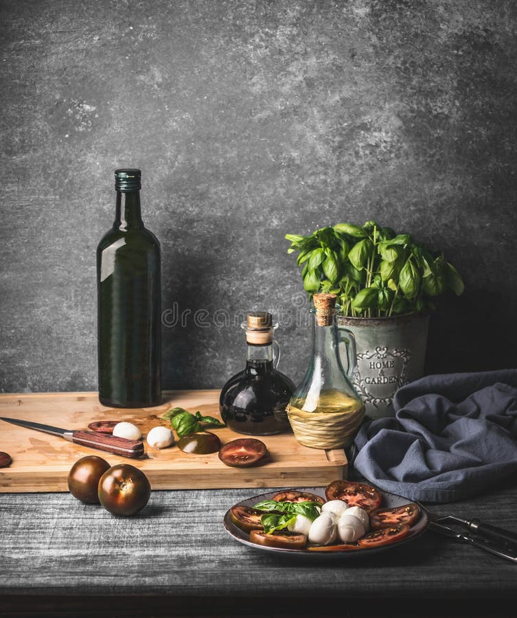 Still life with Italian caprese salad served on rustic table with potted basil kitchen herbs and bottle of olive oil on rustic