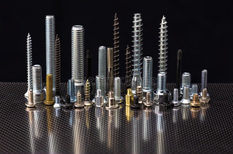 Still life with multi-colored screws, bolts, screws and bushings on a sheet of stainless steel. The screws and bolts are on the caps and look like a night city with skyscrapers