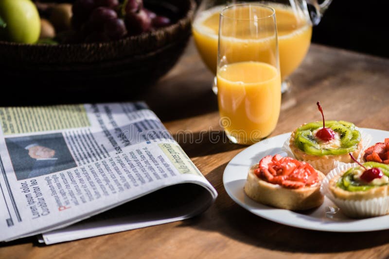 Still life of newspaper, breakfast with cakes and glass of juice