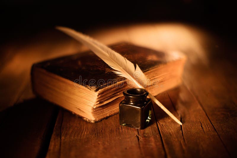 Old book with quill pen and inkwell on wooden table