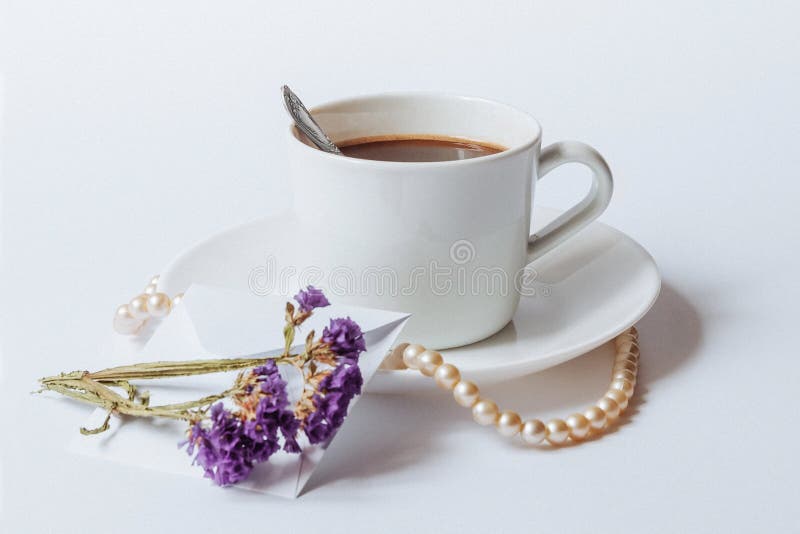 A still life with a white ceramic cup of coffee, a coral necklace, and the dried flowers