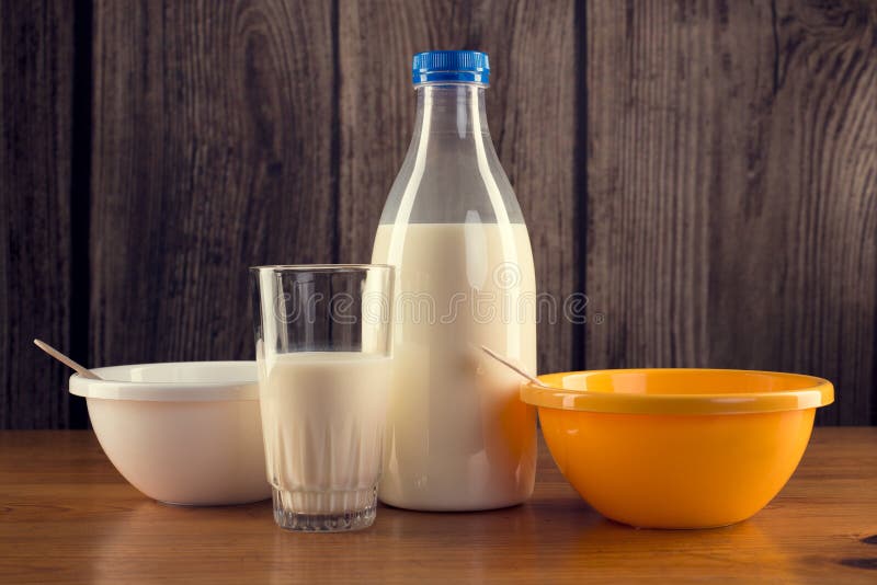 Still life of plastic bottle of milk, glass of milk and two - white and yellow color plastic bowls on wooden table. Over wooden wall background. Still life of plastic bottle of milk, glass of milk and two - white and yellow color plastic bowls on wooden table. Over wooden wall background.