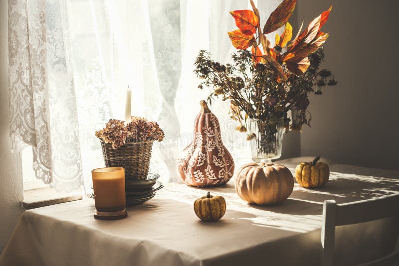 Stillleben im Herbst mit Kürbisdekoration lässt Bunch und Kerze am Tisch und Fensterboden mit weißen Vorhängen und