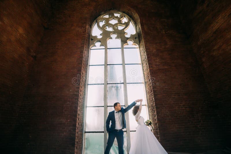 Stilvolle Braut und hübsches elegantes Bräutigamtanzen auf dem Hintergrund des Luxusinnenraums mit großem Fenster lizenzfreie stockfotografie Stilvolle Braut und hübsches elegantes Bräutigamtanzen auf dem Hintergrund des Luxusinnenraums mit großem Fenster lizenzfreie stockfotografie