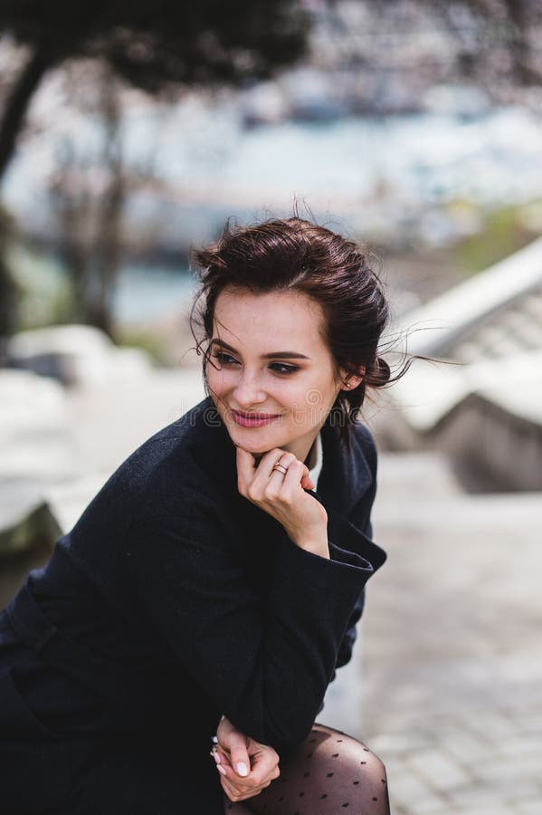 Stilvolle elegante glückliche Frau, die auf der Bank sitzt Sie kleidete im dunklen Mantel und in der Sonnenbrille an stockbilder Stilvolle elegante glückliche Frau, die auf der Bank sitzt Sie kleidete im dunklen Mantel und in der Sonnenbrille an stockbilder