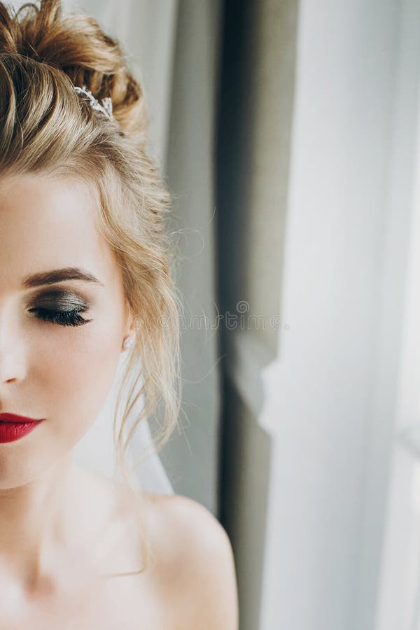 Stilvolle glückliche Braut mit dem überraschenden Make-up, das im weichen Licht nahe Fenster im Hotelzimmer aufwirft Herrliches s stockfoto Stilvolle glückliche Braut mit dem überraschenden Make-up, das im weichen Licht nahe Fenster im Hotelzimmer aufwirft Herrliches s stockfoto