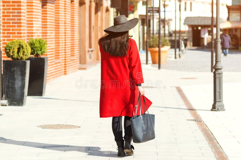Stilvolle schöne Frau, die auf der Straße spaziert Mädchen mit rotem Mantel, schwarzem Hut und angesagter Tasche Mode-Outfit, Her stockfoto Stilvolle schöne Frau, die auf der Straße spaziert Mädchen mit rotem Mantel, schwarzem Hut und angesagter Tasche Mode-Outfit, Her stockfoto
