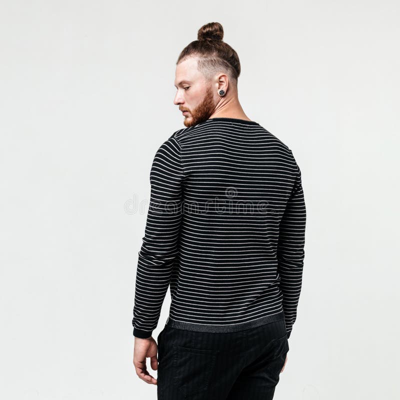 Stilvoller junger Mann mit der Bart- und Brötchenfrisur, die einen dunklen gestreiften Pullover und Hose trägt, wirft Haltungen i lizenzfreie stockbilder Stilvoller junger Mann mit der Bart- und Brötchenfrisur, die einen dunklen gestreiften Pullover und Hose trägt, wirft Haltungen i lizenzfreie stockbilder