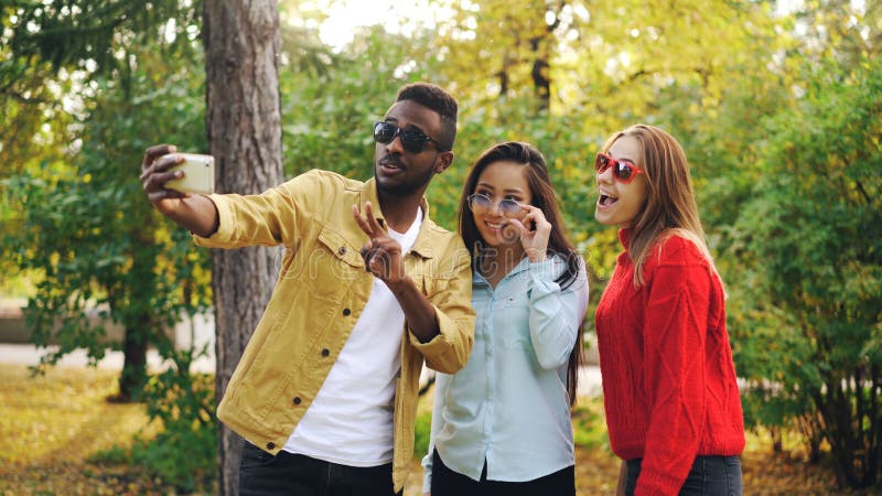 Stilvoller Mann und Frauen der jungen Leute nehmen selfie tragende Sonnenbrille, die Smartphone während halten aufwirft und läche lizenzfreies stockfoto Stilvoller Mann und Frauen der jungen Leute nehmen selfie tragende Sonnenbrille, die Smartphone während halten aufwirft und läche lizenzfreies stockfoto