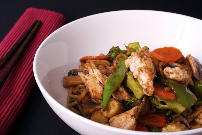 A freshly cooked chicken stir fry with fresh vegetables singapore noodles served in a white bowl with chop sticks. A freshly cooked chicken stir fry with fresh vegetables singapore noodles served in a white bowl with chop sticks