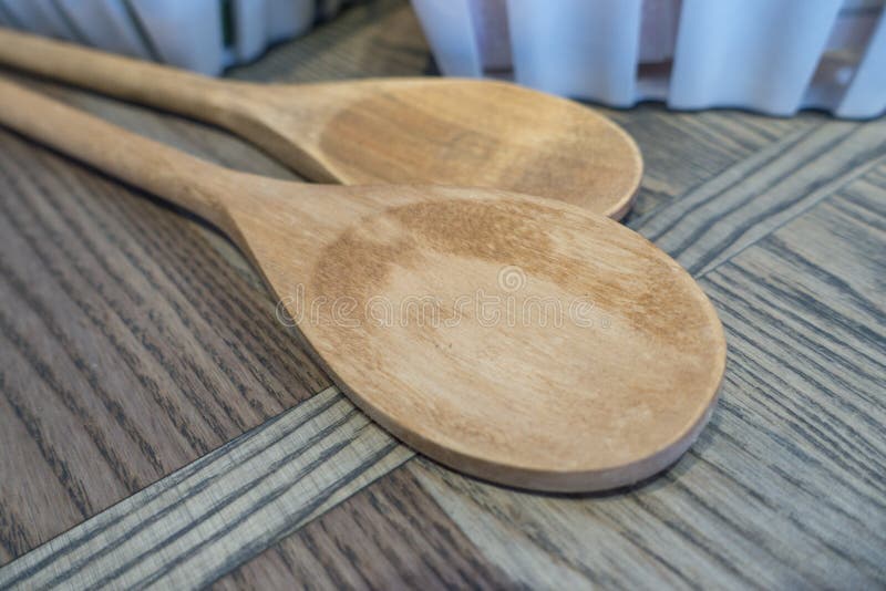 2 light tan wooded spoons on a wood table. 2 light tan wooded spoons on a wood table