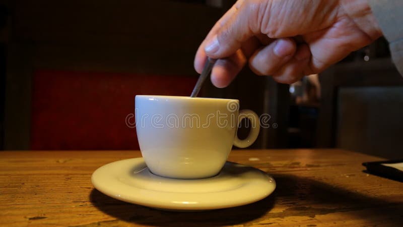 Customer is stirring sugar with teaspoon in the white cup in a dark cafe. Hot cafe video