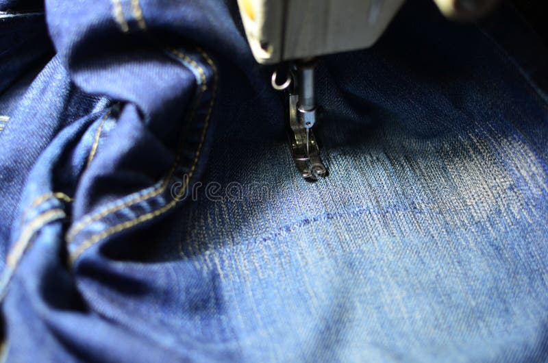 Stitching, stitching a hole in blue jeans with a sewing machine. Part of sewing machine and jeans cloth closeup. stock photography