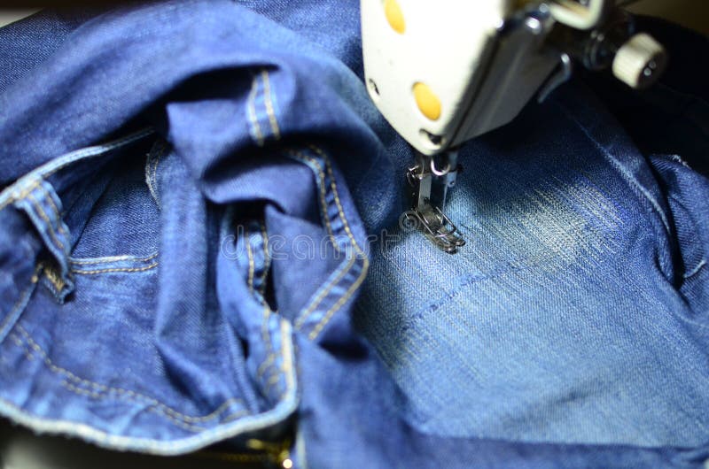 Stitching, stitching a hole in blue jeans with a sewing machine. Part of sewing machine and jeans cloth closeup. royalty free stock photo