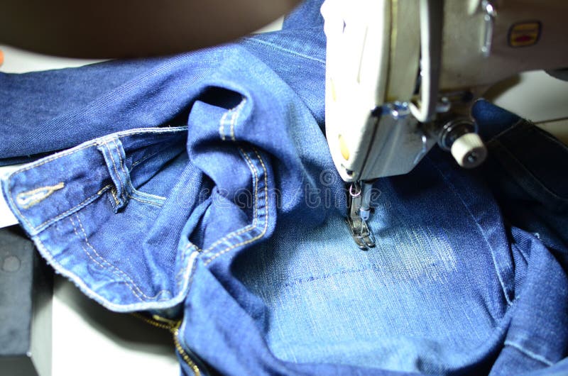 Stitching, stitching a hole in blue jeans with a sewing machine. Part of sewing machine and jeans cloth closeup. stock photos