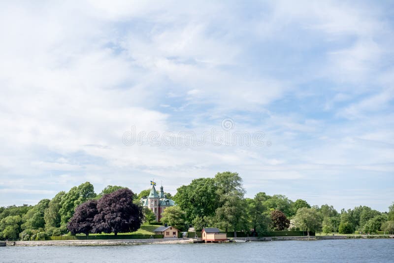 STOCKHOLM, SCHWEDEN - 6. JUNI 2016: Küstenansicht eines alten kleinen Schlosses mit schwedischen Flaggen auf einer Insel von Stoc lizenzfreies stockbild STOCKHOLM, SCHWEDEN - 6. JUNI 2016: Küstenansicht eines alten kleinen Schlosses mit schwedischen Flaggen auf einer Insel von Stoc lizenzfreies stockbild