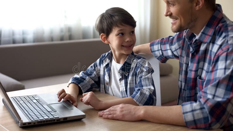 Stolt fader och hans son som direktanslutet shoppar på bärbar datordatoren, teknologier arkivfoto