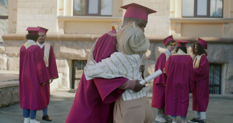 Stolt lärare som pratar med afrikansk man i graderingsgåva och prålande skaka händer