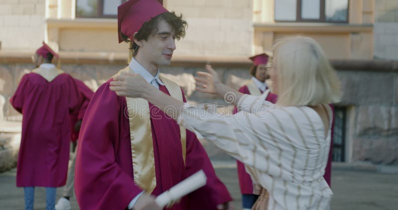 Stolt mor som talar med son på högskoleexamen och som gratulerar med examen på universitetscampus