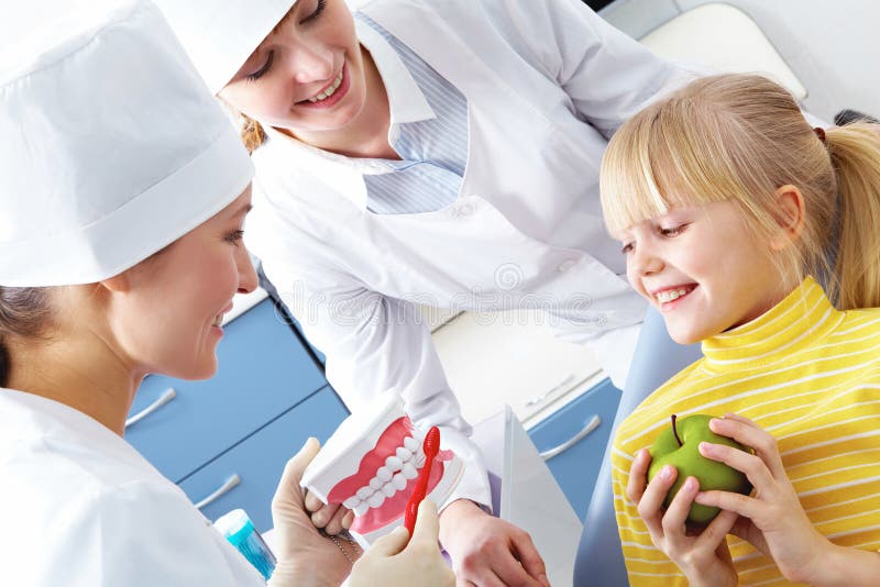 Image of dentist showing care dental hygiene to little girl with assistant near by. Image of dentist showing care dental hygiene to little girl with assistant near by