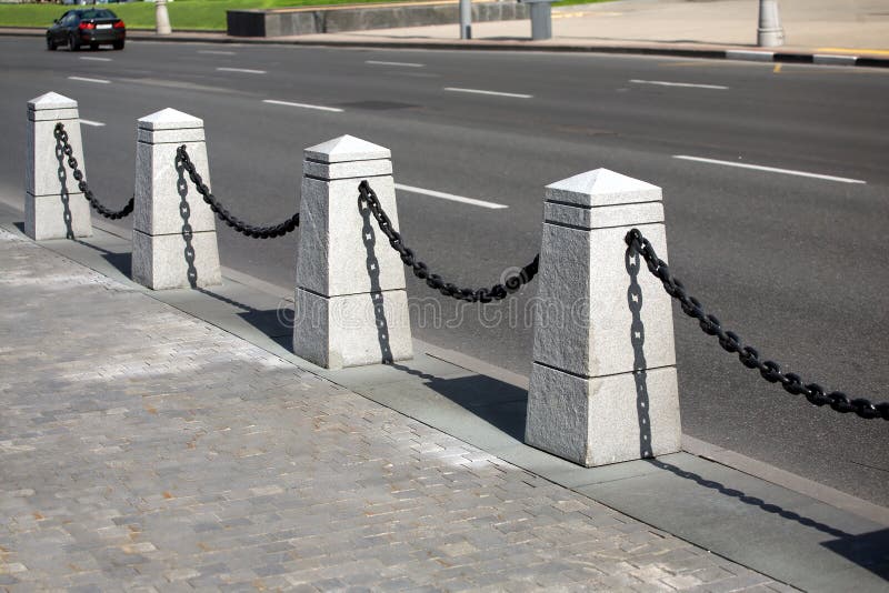 Stone fence with black chain in a city near urban road on summer day