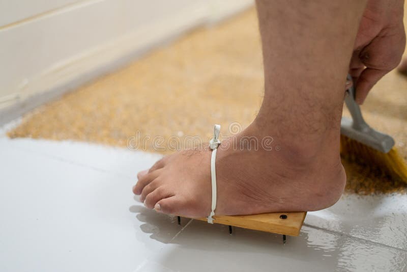 Feet wearing painters& x27; wooden shoes with nails for self leveling epoxy on floor background. Close up. Feet wearing painters& x27; wooden shoes with nails for self leveling epoxy on floor background. Close up