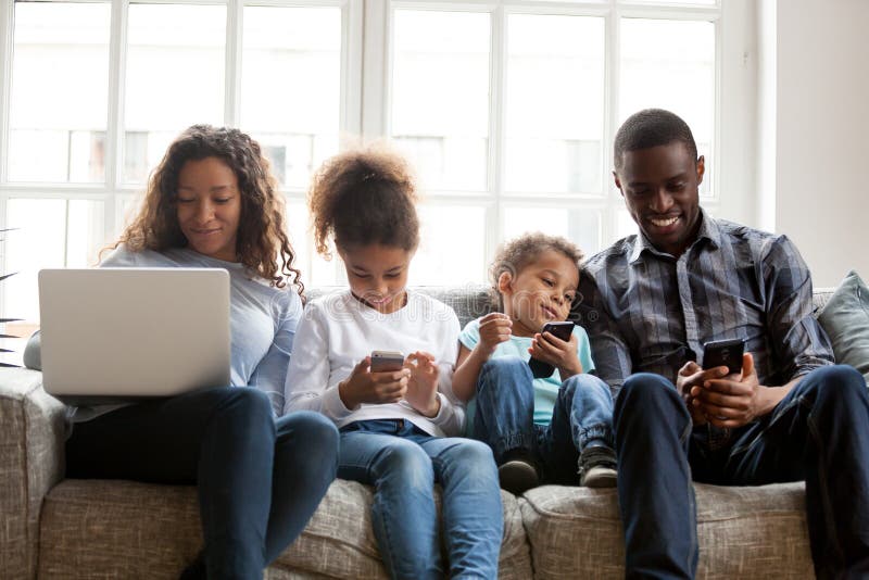 Stor afrikansk amerikanfamilj som använder apparater som tillsammans sitter arkivbild Stor afrikansk amerikanfamilj som använder apparater som tillsammans sitter arkivbild