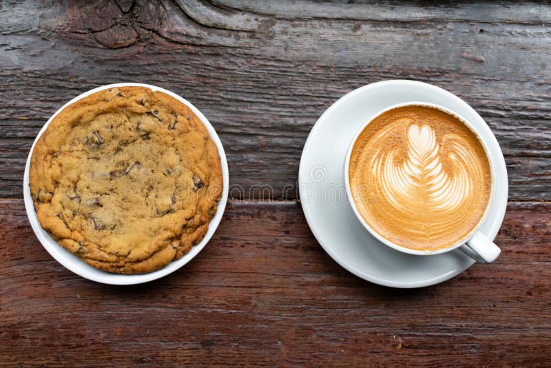 Stor chokladkaka pÃ¥ en platta med en latte pÃ¥ ett träbord arkivfoto