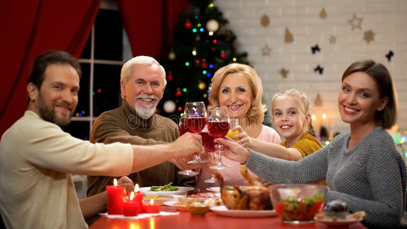 Stor vänlig familj som klirrar exponeringsglas med vin på Xmas-helgdagsaftonen som ser in i kamera royaltyfria bilder Stor vänlig familj som klirrar exponeringsglas med vin på Xmas-helgdagsaftonen som ser in i kamera royaltyfria bilder