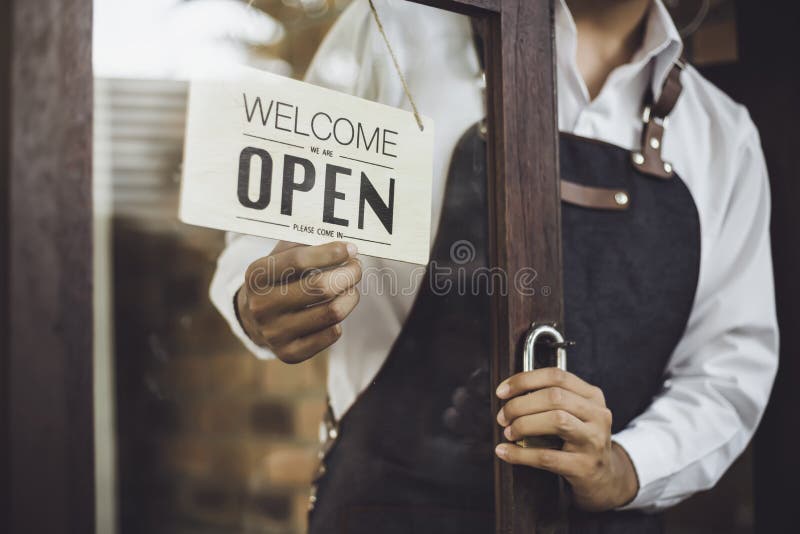 Store owner turning open sign broad through the door glass