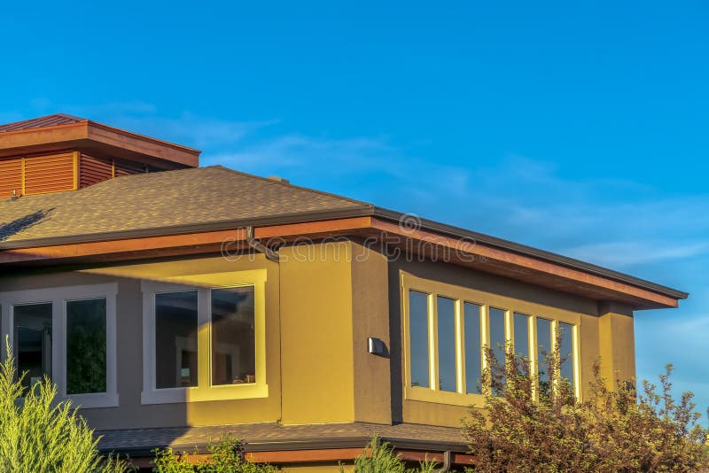 Storia superiore di casa con tetto dell'anca e muro marrone contro cielo azzurro vibrante