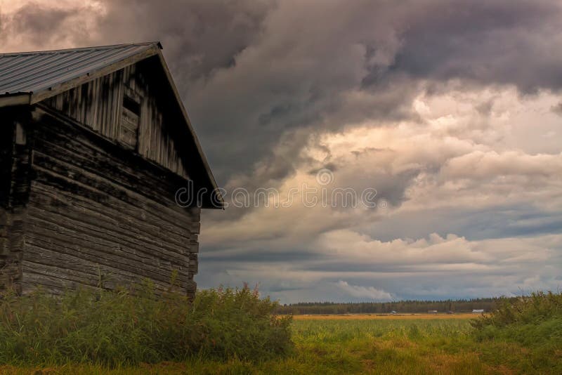 Storm Rising On The Summer Fields. A summer storm is rising on a warm day in the Northern Finland. An old barn stands against the wind and the rain stock photo Storm Rising On The Summer Fields. A summer storm is rising on a warm day in the Northern Finland. An old barn stands against the wind and the rain stock photo