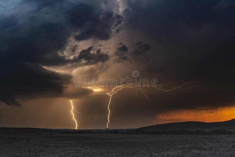 A large lightning strike at dusk in an open plain framed against a deep, dark orange sunset and stormy skies. A large lightning strike at dusk in an open plain framed against a deep, dark orange sunset and stormy skies.