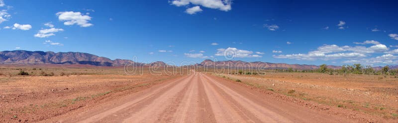 Red, dusty, outback road under the hot sun, heading towards the Flinders Ranges Mountains in the distance. Brachina Gorge, Flinders Ranges National Park, South Australia. Red, dusty, outback road under the hot sun, heading towards the Flinders Ranges Mountains in the distance. Brachina Gorge, Flinders Ranges National Park, South Australia.