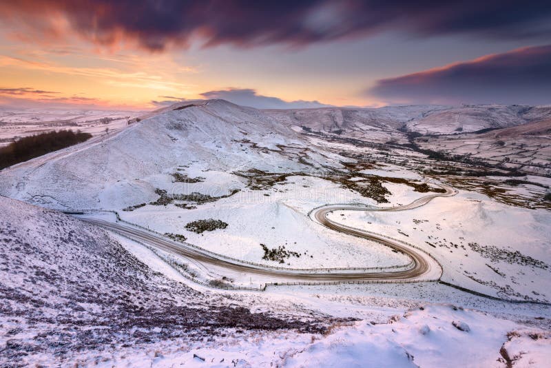 Strada lunga e tortuosa che conduce attraverso la neve ricoperta di neve al tramonto. zona di picco uk.