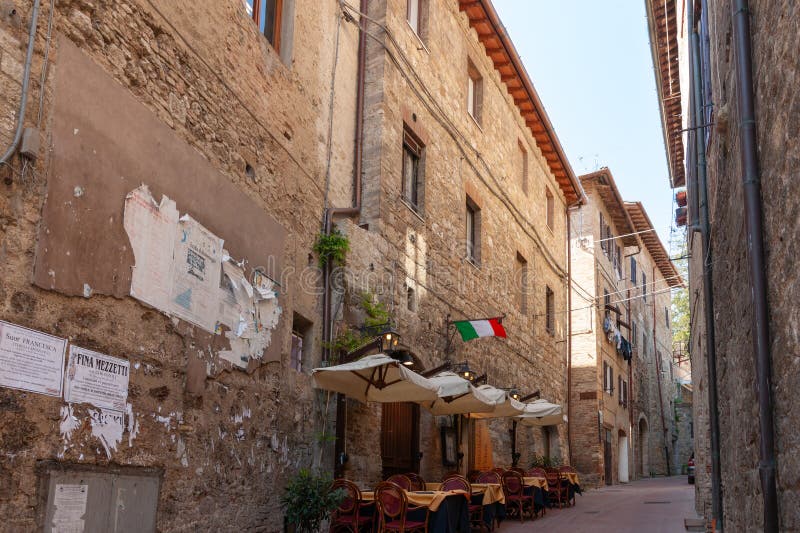 San Gimignano, Italy - April 4 2011 Typical medieval European city streets and buildings with restaurant tables and chairs in street under Italian flag. San Gimignano, Italy - April 4 2011 Typical medieval European city streets and buildings with restaurant tables and chairs in street under Italian flag