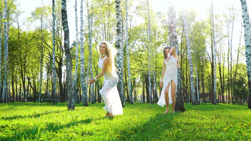 Strahlen des Sonnenlichts auf zwei Frauen in den sexy Kleidern, die barfu? in Birkenwaldung tanzen