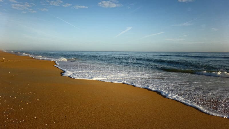 Beach seascape - A photograph showing a golden brown sand perspective of a tropical beach, with gentle white waves coming in from the sea. Beach seascape - A photograph showing a golden brown sand perspective of a tropical beach, with gentle white waves coming in from the sea