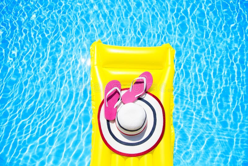 Beach summer holiday background. Inflatable air mattress, flip flops and hat on swimming pool. Yellow lilo and summertime accessories on poolside. Top view and copy space. Beach summer holiday background. Inflatable air mattress, flip flops and hat on swimming pool. Yellow lilo and summertime accessories on poolside. Top view and copy space