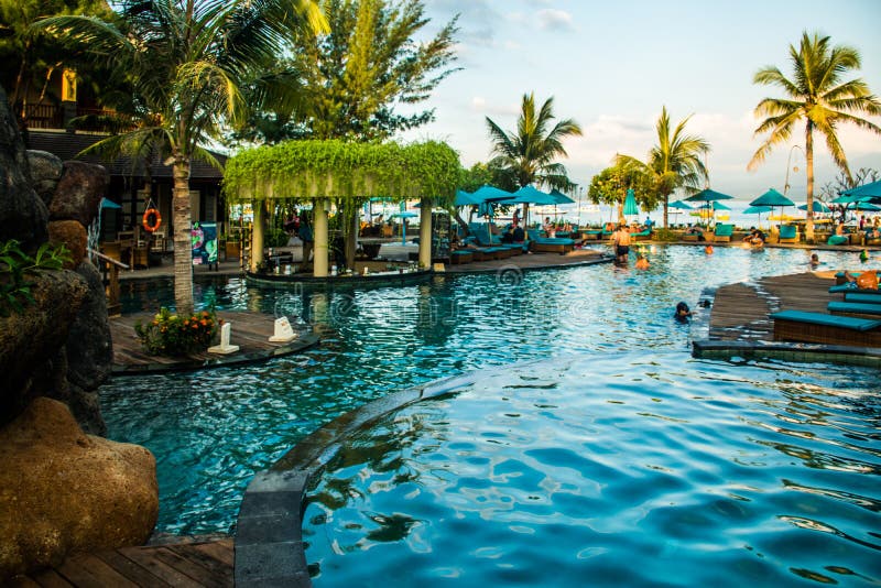 Strandsunbeds nära simbassäng i tropisk semesterort med gömma i handflatan under solnedgången, Gili Trawangan, Lombok, Indonesien arkivbilder Strandsunbeds nära simbassäng i tropisk semesterort med gömma i handflatan under solnedgången, Gili Trawangan, Lombok, Indonesien arkivbilder