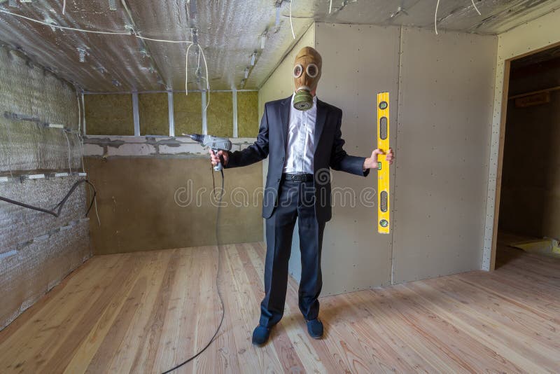 Strange man in businessman suit and gas protection mask inside a room under renovation works holding electric screwdriver and a royalty free stock image Strange man in businessman suit and gas protection mask inside a room under renovation works holding electric screwdriver and a royalty free stock image