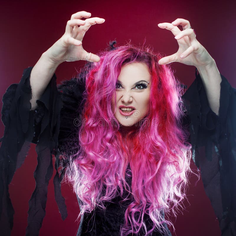 Straszna czarownica z czerwonym włosy wykonuje magię na różowym tle Halloween, horroru temat