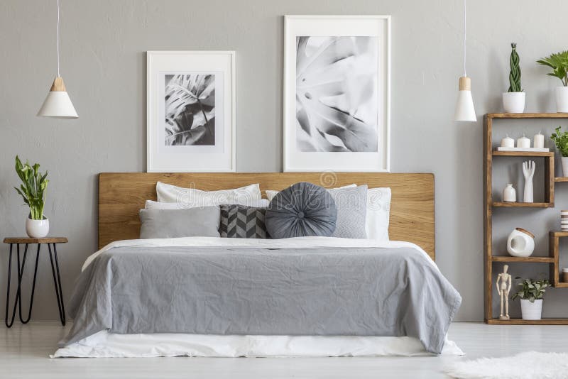 Strati grigi sul letto di legno accanto alla tavola con la pianta nell'interno della camera da letto con i manifesti Foto reale fotografie stock libere da diritti