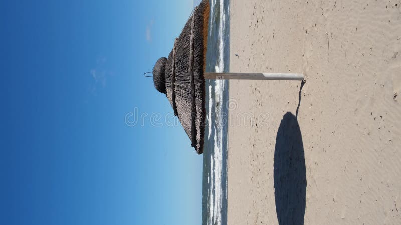 Straw beach rattan parasol at the empty beach with blue sky backgrounds sea ocean coast. Relaxing day. Vertical footage